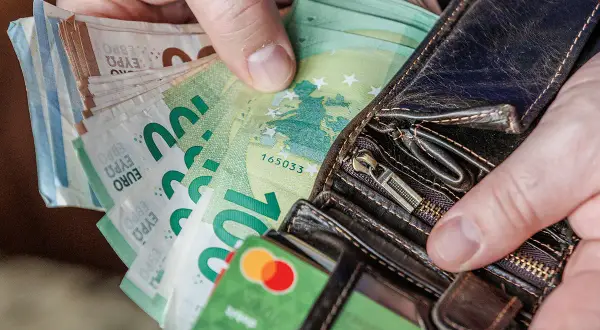 Ręce trzymają portfel z banknotami euro. Widać też kartę debetową. Litwa używa euro jako swojej waluty.