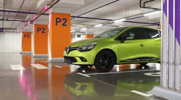 Une voiture verte est garée en bataille dans un parking souterrain, avec des poteaux orange marqués "P2".