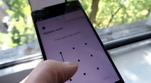 Telefon z ekranem blokady, gdzie wybierasz **wzór** 15 najpopularniejszych blokad. Palec rysuje linię na siatce kropek.