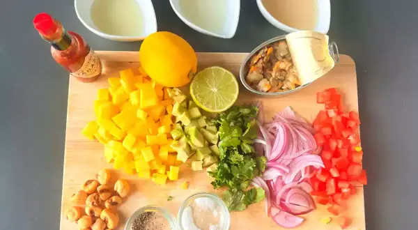 Mise en place para ceviche: mango, aguacate, cebolla morada, tomate, cilantro, limón, lima, mejillones en lata, maíz tostado, Tabasco y líquidos.