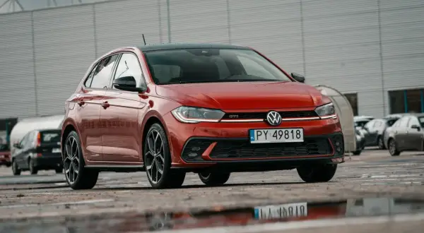 Czerwony Volkswagen Polo GTI z czarnym dachem, zaparkowany na mokrym parkingu.