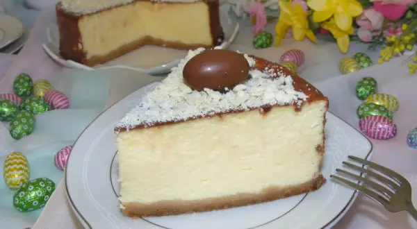 Kawałek kremowego sernika z mascarpone, ozdobiony czekoladowymi jajeczkami i wiórkami białej czekolady, na talerzyku.