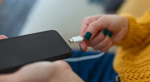 Dłoń z zielonymi paznokciami próbuje podłączyć kabel do telefonu, ale telefon się nie ładuje.
