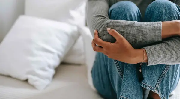 En person sitter hopkrupen på en säng, med armarna runt knäna. Känslan av en panikångestattack i flera timmar kan vara överväldigande.