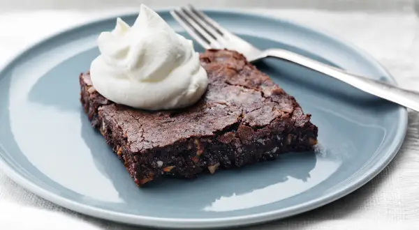 En saftig brownie med nötter, toppad med vispad grädde, redo att avnjutas. Perfekt för ett enkelt brownie recept.
