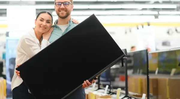 Szczęśliwa para trzyma nowy telewizor. Zastanawiasz się, hisense co to za firma? To producent elektroniki, który oferuje wysokiej jakości sprzęt.