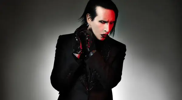 Marilyn Manson zespół w czarnym garniturze, z czerwonym makijażem i rękawiczkami.