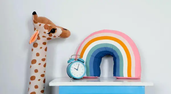 Plüsch-Giraffe, Regenbogen-Kissen und Wecker auf blauem Nachttisch – süße kinderzimmer deko diy.