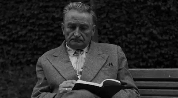 Zamyślony mężczyzna w garniturze czyta książkę na ławce. Może w tej chwili myśli, że życie mnie mnie fraszka, szukając ukojenia w literaturze.