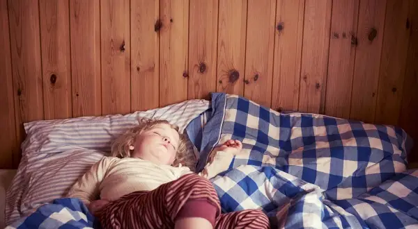 En 3-åring sover i en säng med rutiga täcken. Det är vanligt att en 3-åring kissar på sig på natten.