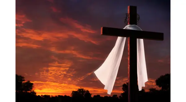 Kreuz mit Dornenkrone und Leichentuch vor dramatischem Sonnenuntergang. Ein Symbol für Karfreitag, den Feiertag der Besinnung.