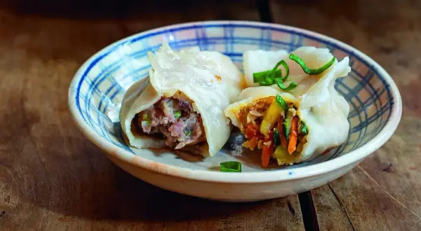 Dwa pierogi gyoza z mięsem i warzywami w miseczce na drewnianym stole.