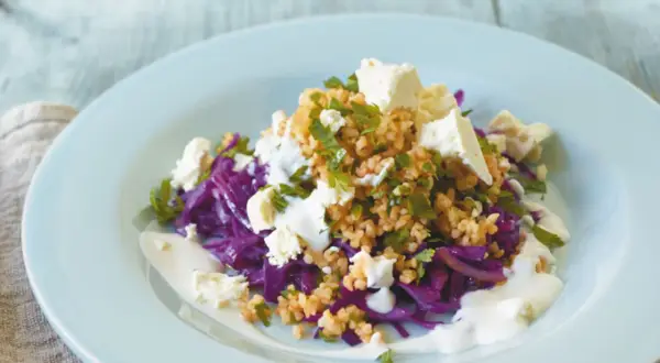 Rotkohl Rezepte mal anders: Ein bunter Salat mit Rotkohl, Bulgur, Feta und Joghurt-Dressing auf einem hellblauen Teller.