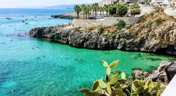 Scogliera con mare cristallino e gente che nuota, tipica dei paesi sul mare in Puglia.