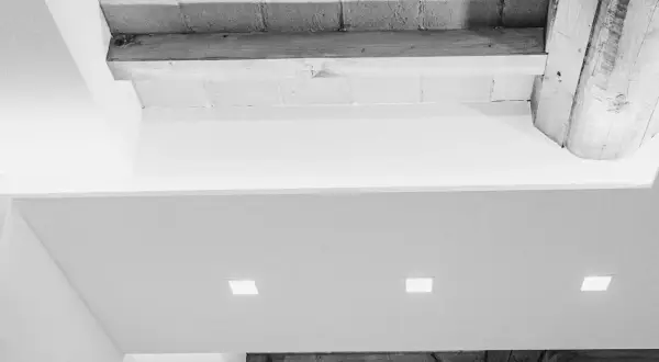 Soffitto con faretti incassati e travi a vista. Una moderna colonna cartongesso con nicchie illumina l'ambiente.
