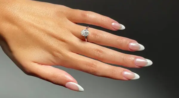 Dłoń z pierścionkiem zaręczynowym i idealnymi paznokciami na zaręczyny. Klasyczny french manicure podkreśla blask kamienia.