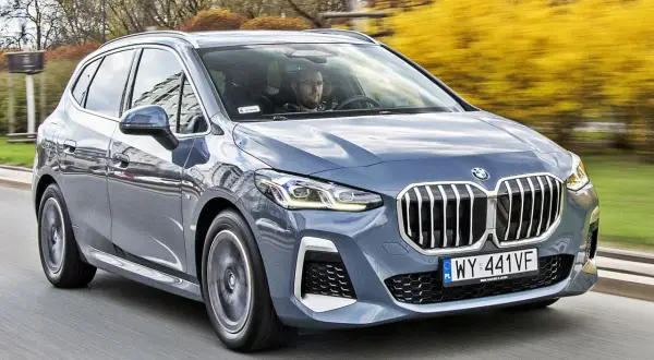 Szary BMW 2 Active Tourer jedzie po drodze, za nim widać żółte krzewy.