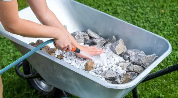 Beim **gartenbrunnen selber bauen** werden Steine in einer Schubkarre mit Wasser abgespült.