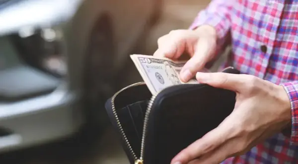 Ręce wyciągają banknot 50 dolarów z portfela, przygotowując się do kupna samochodu od osoby prywatnej.