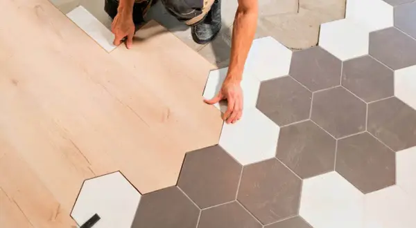 Ręczne łączenie paneli podłogowych z płytkami ceramicznymi w kształcie heksagonów, tworząc płynne przejście bez widocznej listwy progowej.