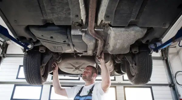 Mechanik sprawdza podwozie sedana na podnośniku, badając układ wydechowy i zawieszenie.