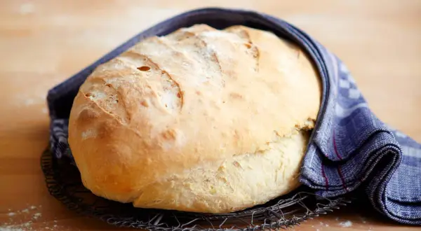 Frisch gebackenes Brot, das nach dem **Brot selber backen** auf einem Gitter abkühlt. Ein blau-weißes Tuch umhüllt es.