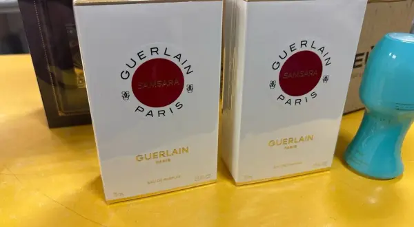 Dwie białe perfumy Samsara Guerlain 75 ml, każda w złotym opakowaniu, stoją na żółtej powierzchni.