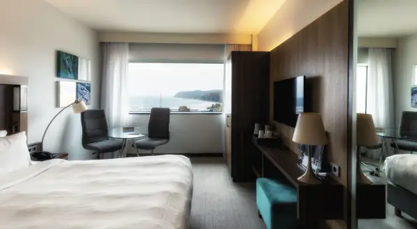 Pokój w hotelu Marriott Gdynia z widokiem na morze. Wygodne łóżko, stolik z krzesłami i telewizor.