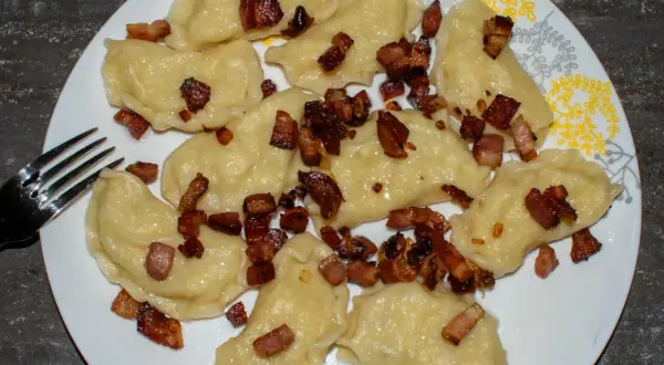 Pyszne pierogi galicyjskie z chrupiącym boczkiem na talerzu. Obok leży widelec.