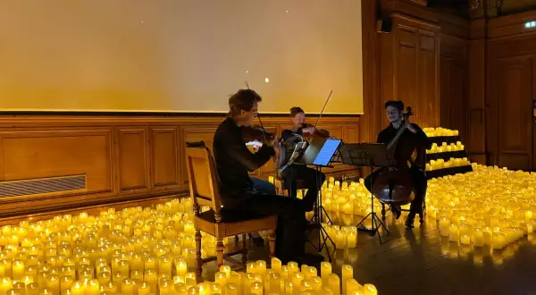 Un trio de musiciens joue dans une salle baignée par la douce lueur de milliers de bougies. Un concert à la bougie magique.