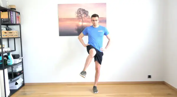 Homme effectuant un exercice de rotation interne hanche, jambe levée, mains sur les hanches.