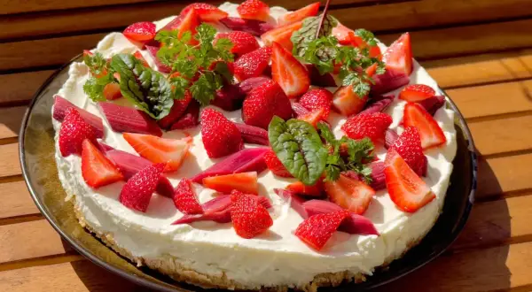 Ein köstlicher Erdbeer Rhabarber Kuchen mit frischen Früchten und Kräutern, bereit zum Genießen.