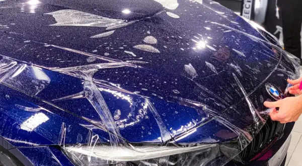 Niebieski **car color** z folią ochronną na masce. Widać krople wody i pęcherzyki powietrza pod folią.