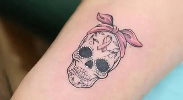Calavera adornada con lazo rosa y cinta de concienciación, símbolo de tatuajes de superación cáncer.