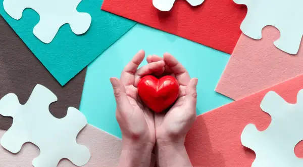 Mani che stringono un cuore rosso, circondate da pezzi di puzzle bianchi e sfondi colorati. Un gesto d'amore, perché si può fare una donazione tra fratelli.