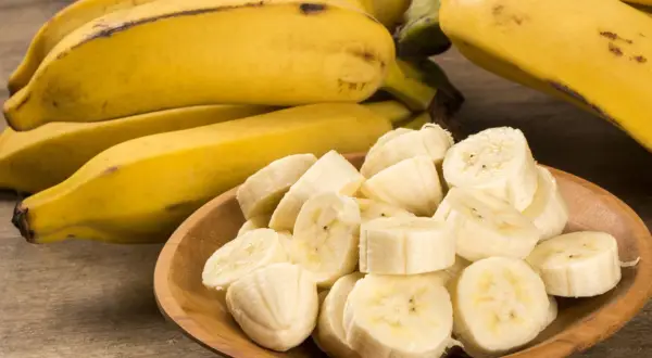 Kawałki banana na drewnianej misce, obok całe owoce. Idealna przekąska, gdy zastanawiasz się nad banan kcal.