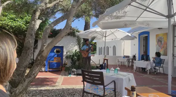 Un músico toca la guitarra en el patio de el pozo de los frailes restaurantes. Mesas puestas bajo sombrillas blancas invitan a disfrutar.