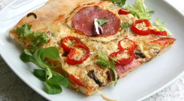 Kawałek pizzy z salami, papryką i serem na białym talerzu. Idealne ciasto na pizzę z chrupiącymi brzegami.