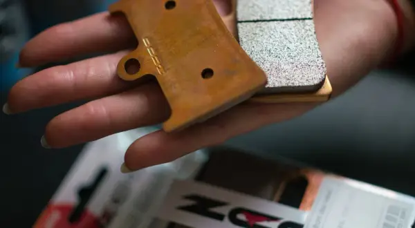 Main d'une personne tenant des plaquettes de frein neuves, prêtes pour le rodage. Le logo "DZ" est visible sur l'une d'elles.