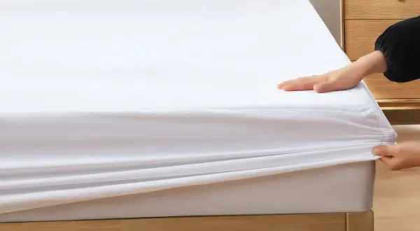 Dłonie naciągają białe prześcieradło na materac, pokazując, jak dopasowuje się ono do różnych rozmiarów prześcieradeł.