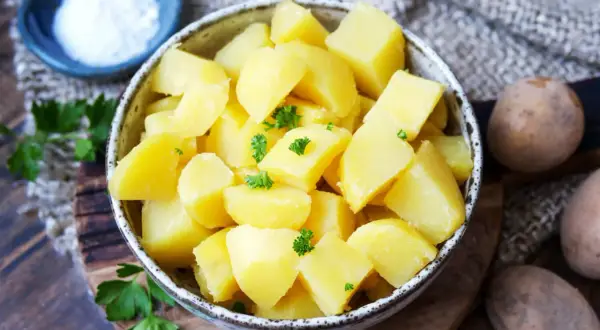 Schüssel mit dampfenden Salzkartoffeln, garniert mit Petersilie. Daneben eine kleine Schale Salz und rohe Kartoffeln.