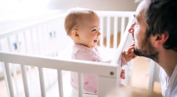 Een lachende baby in een ledikantje reikt naar de baard van haar vader. Pure liefde tussen vader en dochter.