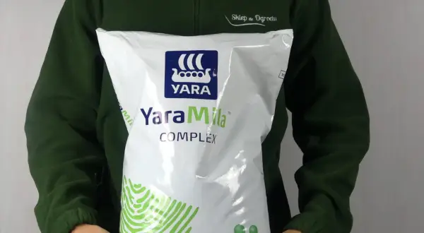 Osoba w zielonej bluzie trzyma worek nawozu YaraMila COMPLEX. Na opakowaniu widnieje logo YARA i informacja o wadze 10 kg.