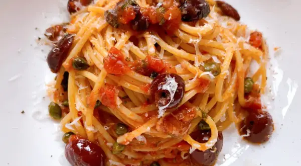 Ein Teller Spaghetti Puttanesca, garniert mit Oliven, Kapern und geriebenem Parmesan.