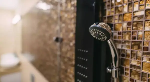 Une colonne de douche moderne avec un pommeau chromé et des jets intégrés, prête à installer dans une salle de bain aux murs mosaïqués.