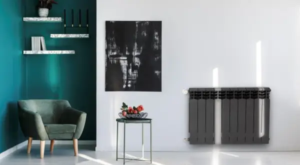 Nowoczesny grzejnik stalowy czy aluminiowy? W stylowym salonie z zieloną kanapą i abstrakcyjnym obrazem, ciemnoszary grzejnik dodaje elegancji.