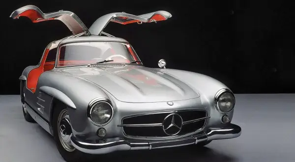 Srebrny Mercedes 300SL z otwieranymi do góry drzwiami, z czerwonym wnętrzem, prezentuje się elegancko na ciemnym tle.