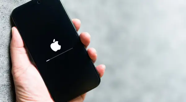 Dłoń trzyma iPhone'a z logo Apple i paskiem postępu. To może być wskazówka, jak wyczyścić pamięć w iPhone, gdy system się ładuje.