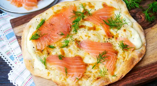 Flammkuchen mit Lachs und Dill, frisch gebacken auf einem Holzbrett.