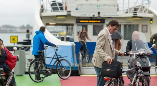 Man met fiets op veerboot, een ongeluk fietser in de verte.